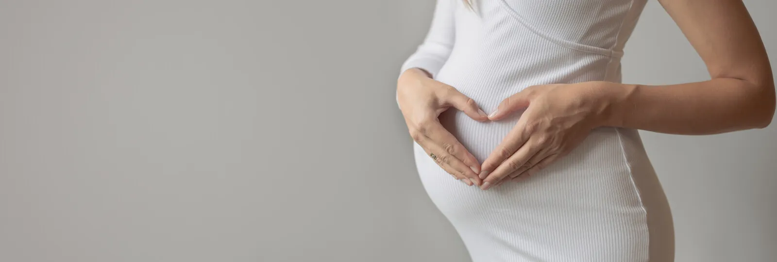 a pregnant woman making a heart with her hands on her belly
